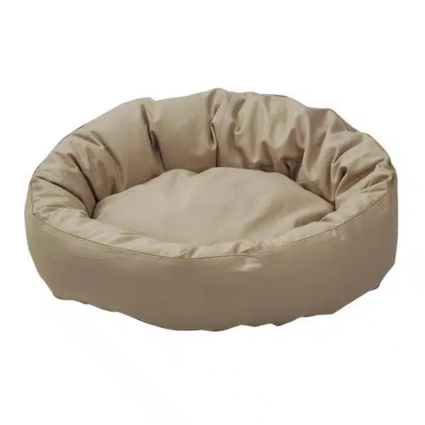 Ein ovales Hundebett mit sandfarbenem Bezug. Der Rand und die Liegefläche wirken bauschig und weich.