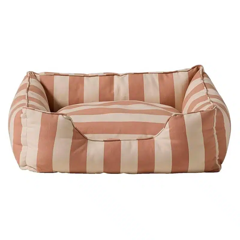 Ein Hundebett in klassischer Form mit erhöhtem Rand und niedrigem Einstieg. Bezug aus breit beige und altrosa gestreiftem Baumwoll-Canvas